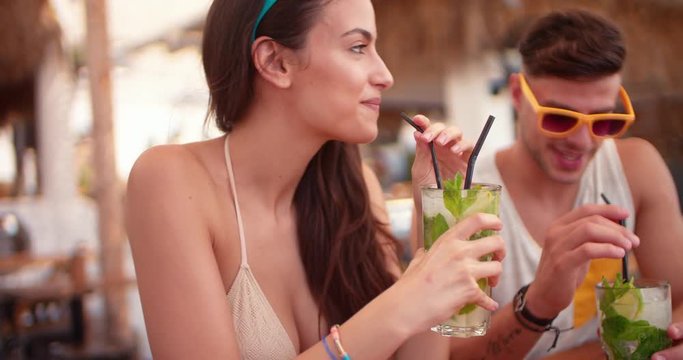 Young man and woman drinking cocktails at tropical beach bar