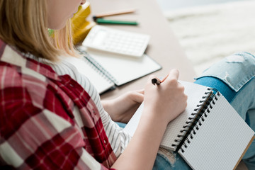 cropped shot of teen student girl writing in notebook while sitting on couch