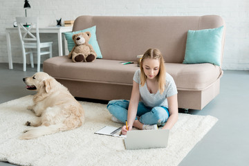 teen student girl doing homework while sitting on floor with her dog