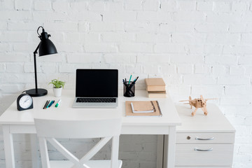 work desk with laptop at home in front of white brick wall