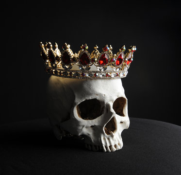 portrait of a human skull wearing golden crown, photographed on black studio background.