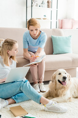 mother and teen daughter doing homework together while their golden retriever lying on floor