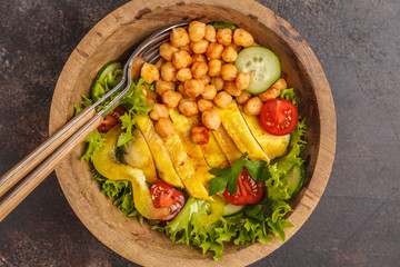 Grilled chicken salad with vegetables and chickpeas in a wooden bowl on a dark background. Healthy balanced diet concept.
