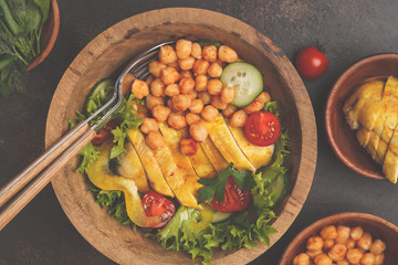 Grilled chicken salad with vegetables and chickpeas in a wooden bowl on a dark background. Healthy balanced diet concept.