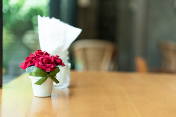 Fake red rose in white pot on wooden table