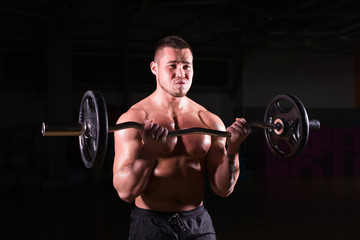 Naklejka na ściany i meble Muscular young man lifting weights on dark background