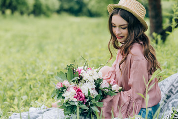 side view of beautiful smiling woman with bouquet of flowers resting on blanket in park