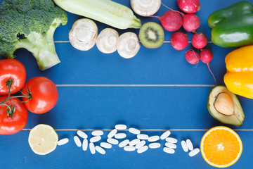 Healthy food,organic fruit and vegetable, nutrition supplement opposite pills and colorful medicines on blue wooden background. Healthy fruits diet as an alternative to multivitamin complex in tablets