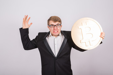 Portrait of a angry businessman holds big golden bitcoin in his arms. Man in panic of cryptocurrency crash
