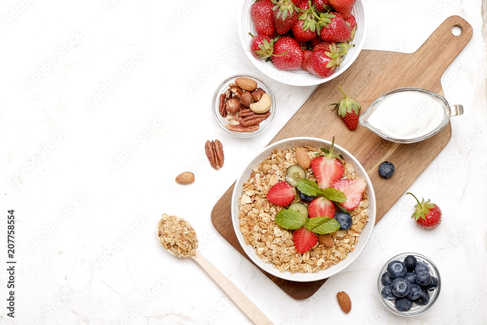 Wall mural Serving option of granola bowl with mix of nuts, cereals, fruits and berries, greek yogurt. Healthy vegetarian breakfast, organic strawberry, blueberry, mint, almond. Close up, top view, background.