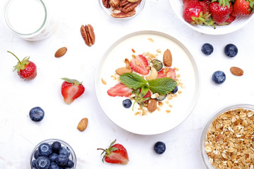 Serving option of granola bowl with mix of nuts, cereals, fruits and berries, greek yogurt. Healthy vegetarian breakfast, organic strawberry, blueberry, mint, almond. Close up, top view, background.