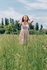 Naklejka na ściany i meble portrait of young beautiful woman in stylish dress standing in meadow alone