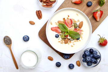 Serving option of granola bowl with mix of nuts, cereals, fruits and berries, greek yogurt. Healthy vegetarian breakfast, organic strawberry, blueberry, mint, almond. Close up, top view, background.