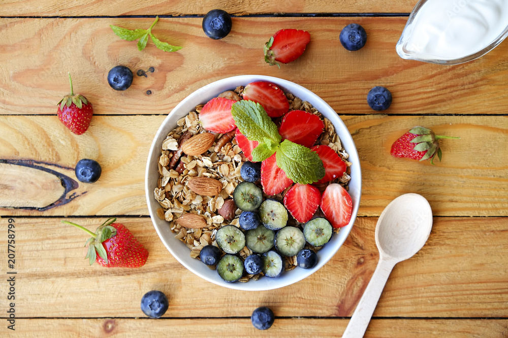 Wall mural Serving option of granola bowl with mix of nuts, cereals, fruits and berries, greek yogurt. Healthy vegetarian breakfast, organic strawberry, blueberry, mint, almond. Close up, top view, background.