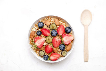 Serving option of granola bowl, mix of nuts, cereals, fruits & berries, greek yogurt, spoon. Healthy vegetarian breakfast, organic strawberry, blueberry, mint, almond. Close up, top view, background.