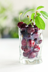 Ripe and fresh burgundy cherries in a glass vase on a background of trees and the sun