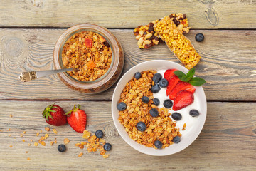 Bowl of homemade granola with yogurt and fresh berries on wooden background