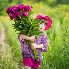 little girl in hat holding huge crimson peonies. warm summer Sunny day outside the city outdoors