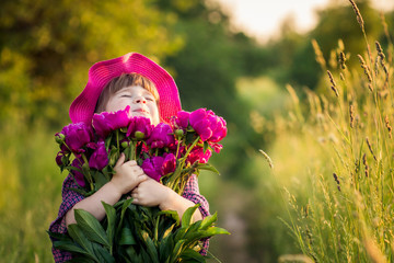a little girl in a hat presses a large bouquet of crimson peonies. warm summer Sunny day outside the city outdoors