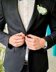Groom in white shirt and black suit with boutonniere buttonning his jacket at wedding day indoors, close-up. Business man dressing up. Fashion, style, lifestyle