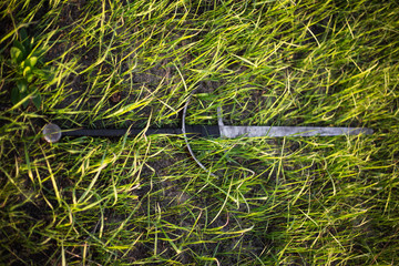 a two-handed sword lies in a tall green grass. The battlefield, after the battle. Crusade, medieval weapons. Lost, forgotten sword, fallen warrior.
