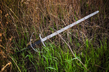 a two-handed sword lies in a tall green grass. The battlefield, after the battle. Crusade, medieval weapons. Lost, forgotten sword, fallen warrior.