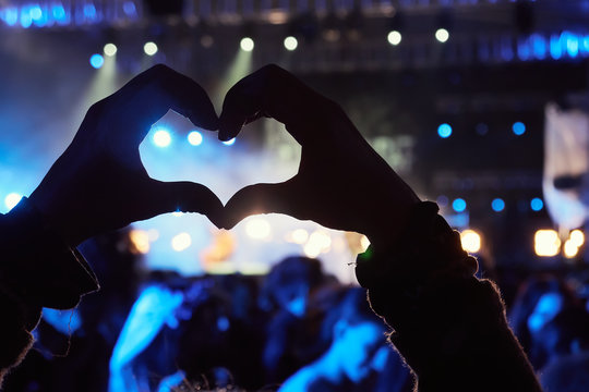 Girl making a heart-shape symbol, enjoying live music festival