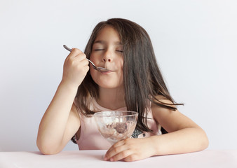 Happy child girl eating ice cream in white and chocolate bowl on white background. Enjoying delicious.