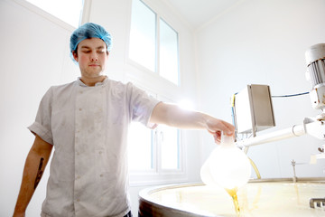 Cheese maker adding rennet to curdle cheese in vat