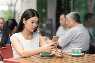 Businesswoman sitting outdoors, at cafe, using smartphone