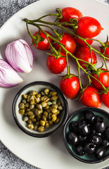 Mediterranean food salad ingredients on a plate on a stone table. Red onion, olives, capers and cherry tomatoes with olive oil. Healthy food