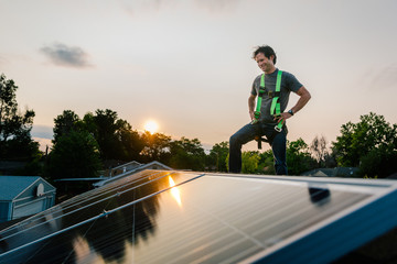 Workman standing on roof of house, installing solar panels