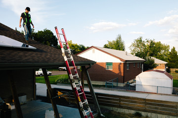 Workman standing on roof of house, installing solar panels