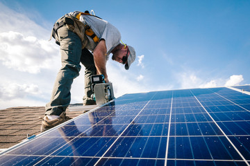 Workman installing solar panels on roof of house, low angle view