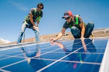 Two workmen installing solar panels on roof of house, low angle view