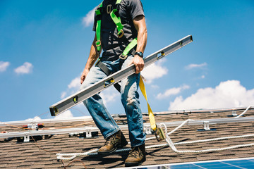 Workman installing solar panels on roof of house, holding spirit level, low section, low angle view