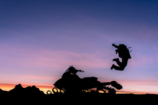 Silhouette of person jumping for joy, beside parked motorbike, at sunset, Whistler, British Columbia, Canada