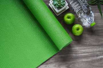 Green yoga mat on a wooden background with green apples and bottle of water. Active healthy lifestyle background concept.