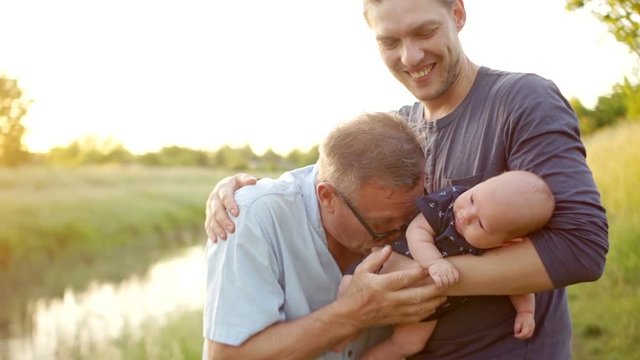 Three generations of men. Grandpa, father and little grandson. Father and son greet each other with a handshake. Sunset, the bank of the river