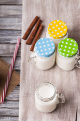 Milk jars with colorful caps on a cutting board, cinnamon and drinking straw 