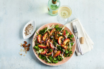 summer, very tasty salad with peaches, sweet onions and arugula with almonds on a table in a plate. simple healthy recipe and a bottle with a glass of white wine