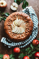 top view of arranged apple pie and fresh apples with green leaves on wooden surface