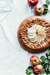 top view of arranged apple pie, fresh apples and green leaves on white tablecloth