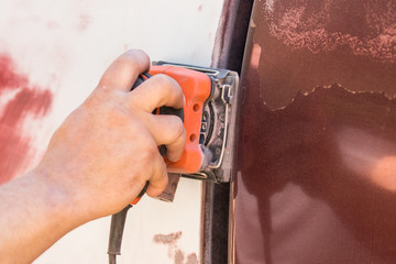 Male hand using a palm sander on a vehicle to remove paint