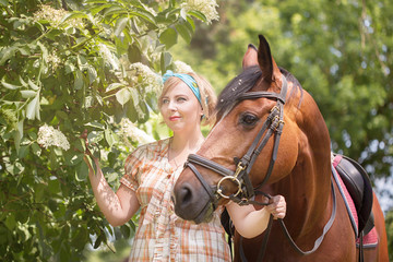 Cheerful, beautiful blonde girl walks in summer sunny weather in a forest by the river with a horse
