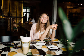 Young blond lady drinking coffe and looking aside through a window.