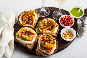 snack breads with hummus and baked pumpkin on a serving board with arugula pesto. seeds of pomegranate and pine nuts. healthy food