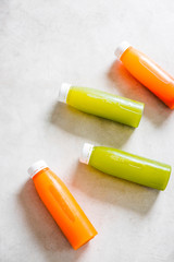 Plastic bottles of cold-pressed fruit and vegetable juices, white plate with mini carrots, kiwi and oranges. From above, light gray table. Body cleance, fast, healthy snacks concept.