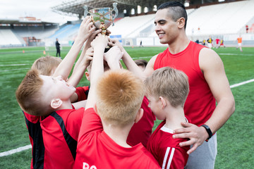 Portrait of junior football team holding trophy together and cheering after winning match in...