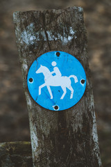 Bridle path round blue sign on a wooden stake, with blurry land path in the background. Germany